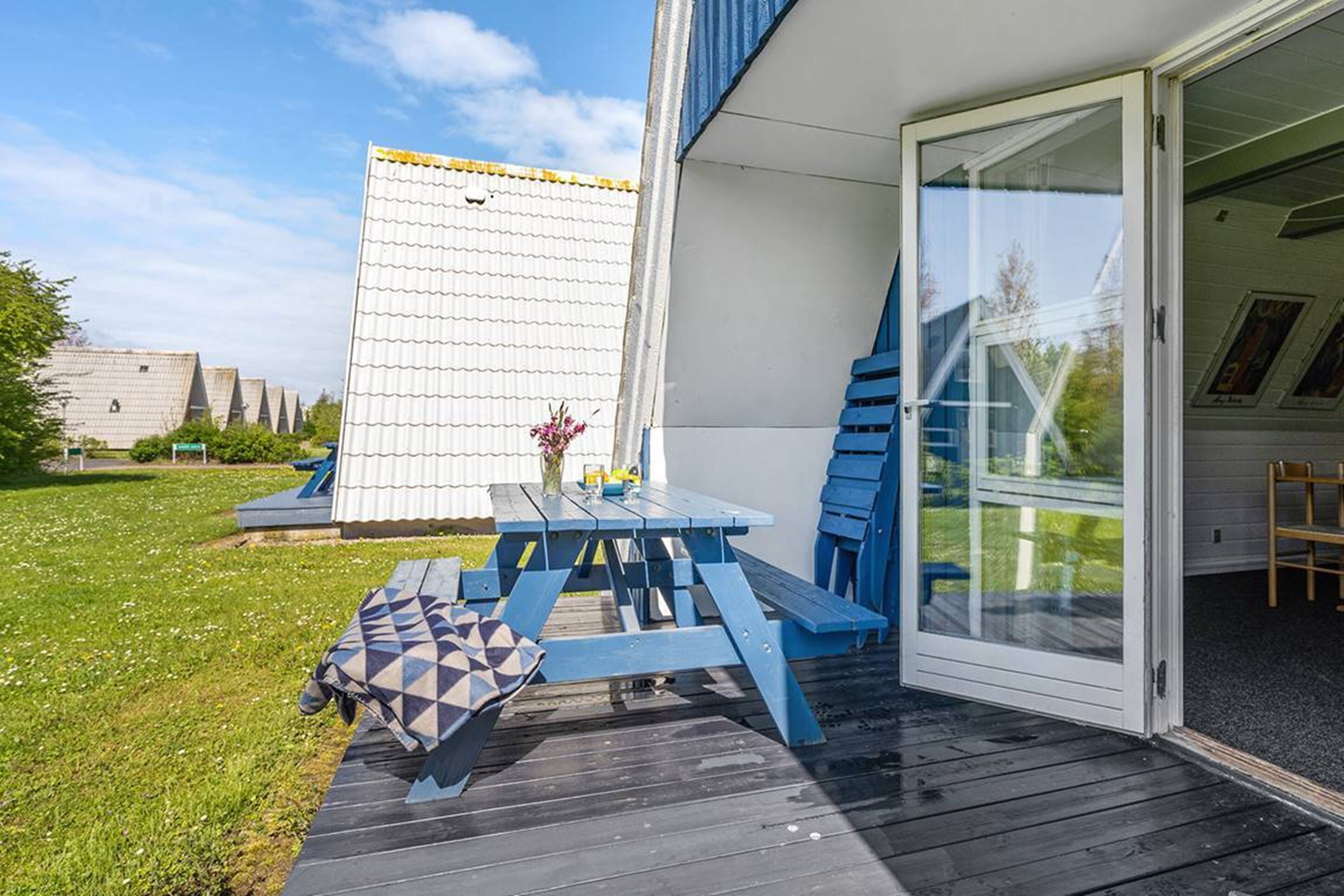 A patio with a wooden table and chairs, a small garden area, and a building with a white exterior and a glass door.