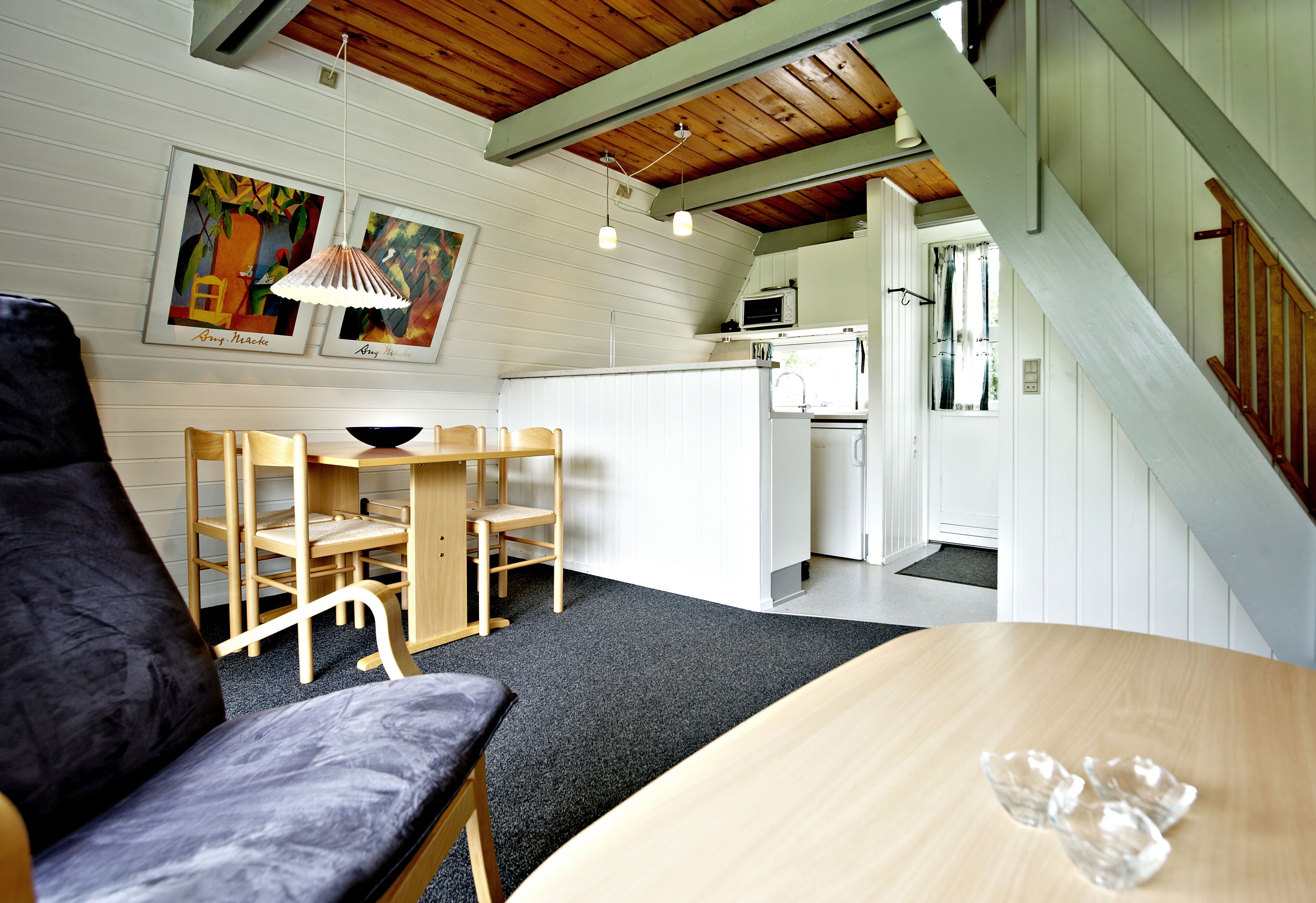 Una habitación acogedora con una mesa de madera, un banco acolchado y una zona de cocina con microondas.