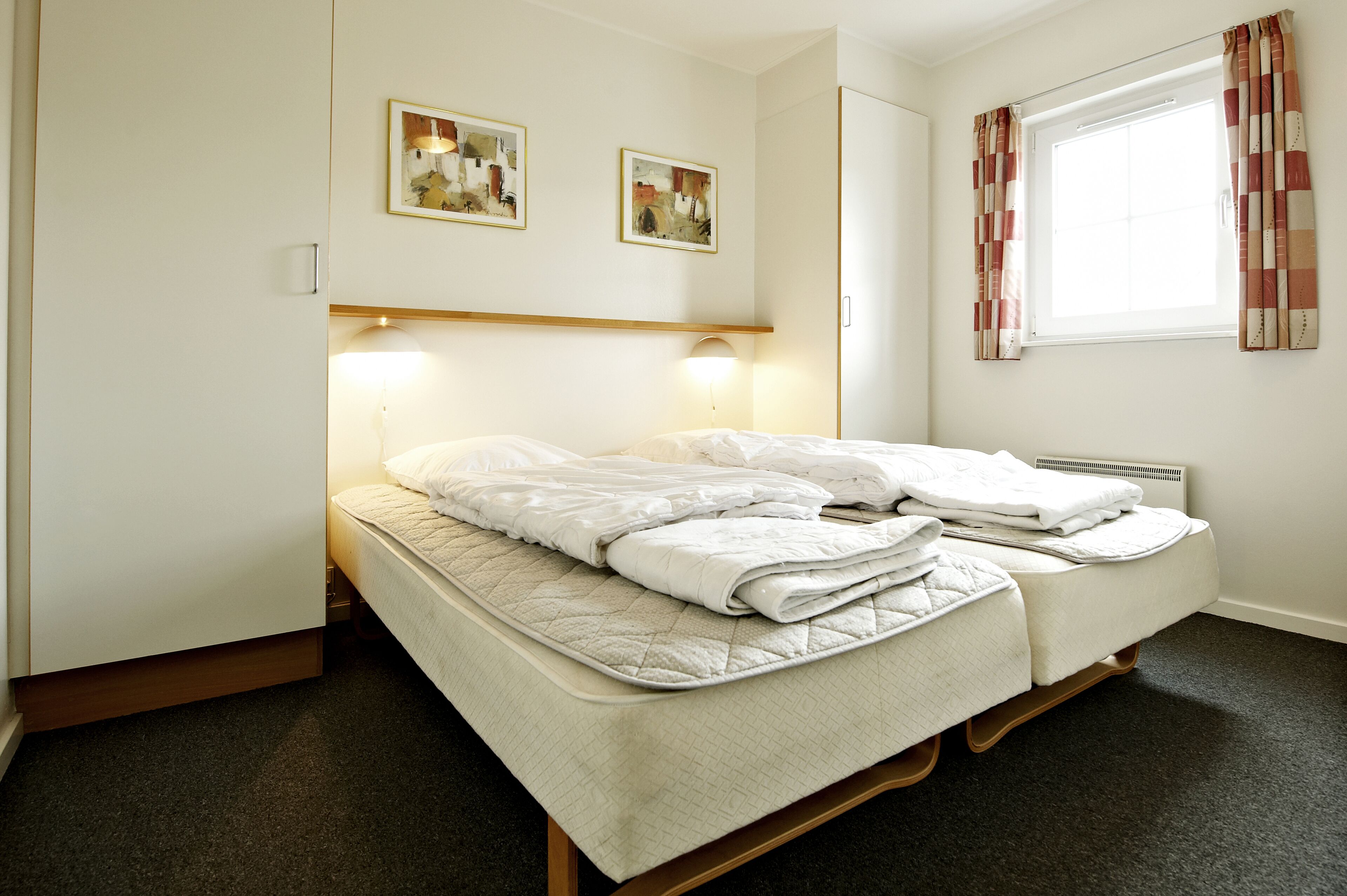 A double bed with a quilted mattress, two bedside lamps, and a window with curtains.