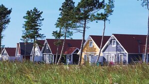 Une rangée de maisons de plage aux toits rouges et aux façades blanches, entourées d’herbes hautes et d’arbres.