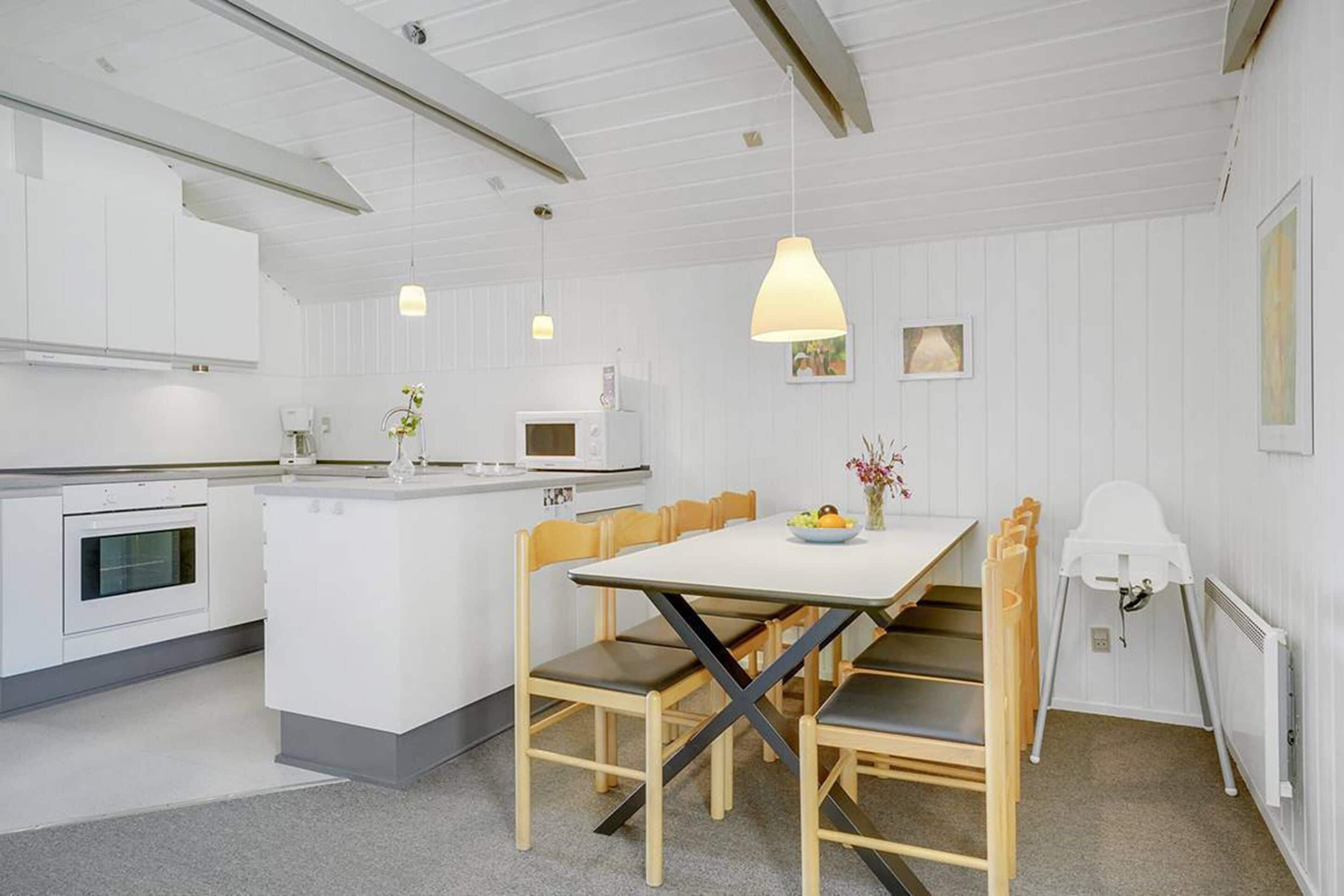 A modern kitchen with white cabinetry, a central island, and a dining area with wooden chairs and a white table.