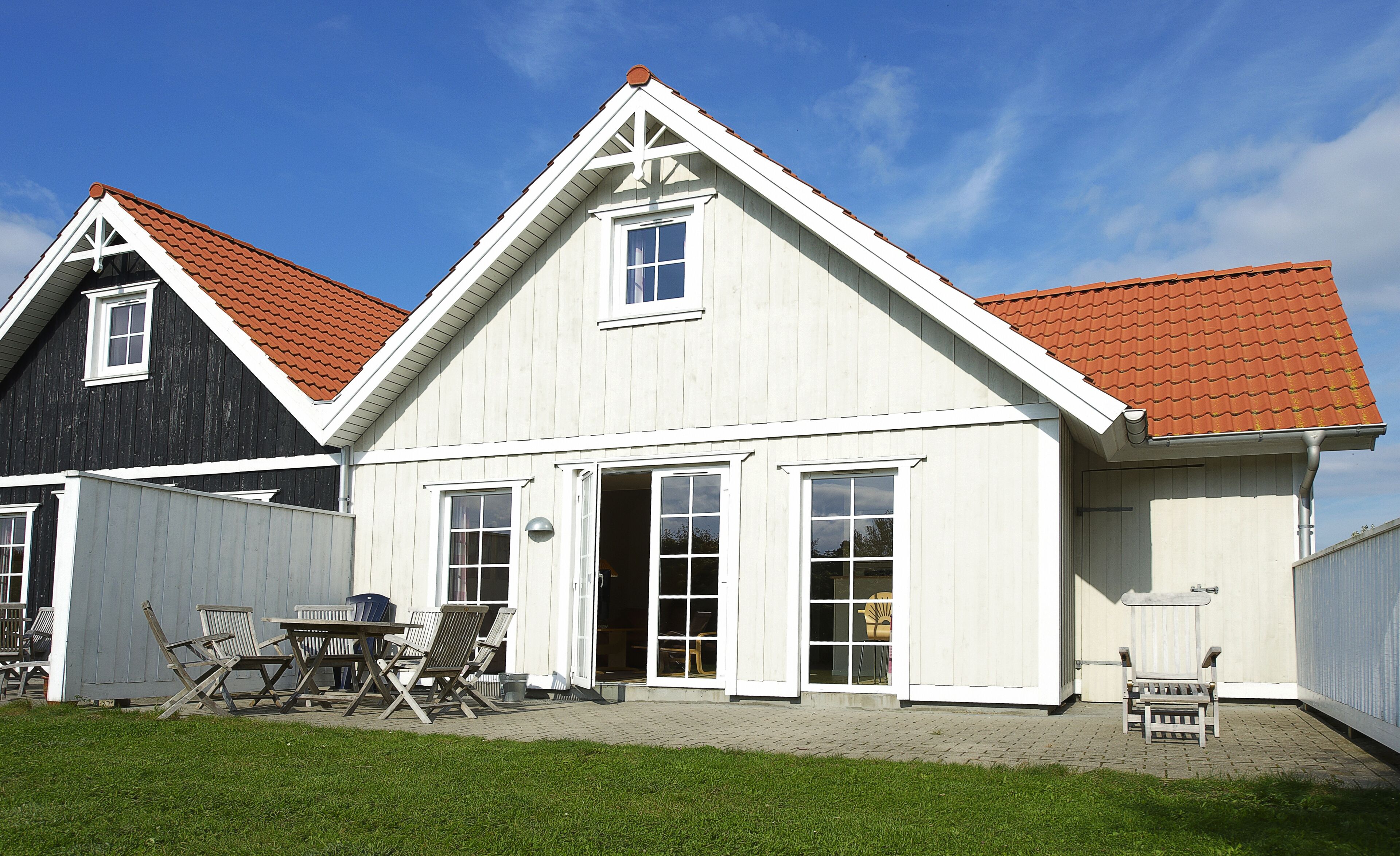 A two-story house with a red-tiled roof and white trim. There is a patio with outdoor furniture and a grassy lawn in front.