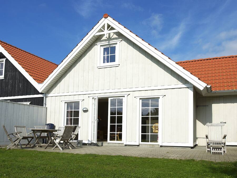 A two-story house with a red-tiled roof and white trim. There is a patio with outdoor furniture and a grassy lawn in front.