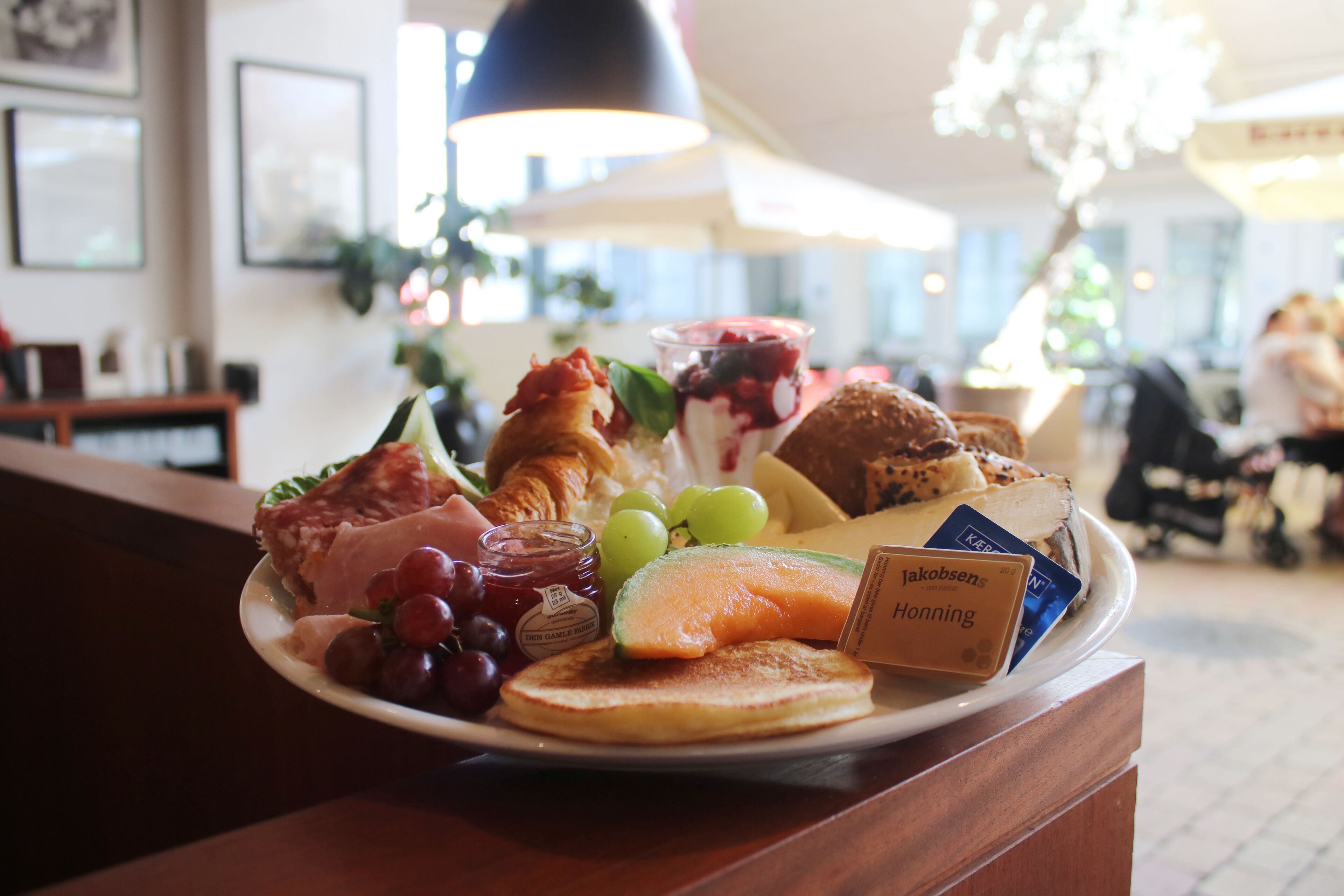 A breakfast plate with various foods including ham, grapes, a croissant, and a slice of bread.