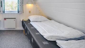 Ein Einzelbett mit weißer Bettwäsche, ein Nachttisch mit Lampe und ein Fenster mit Vorhängen.