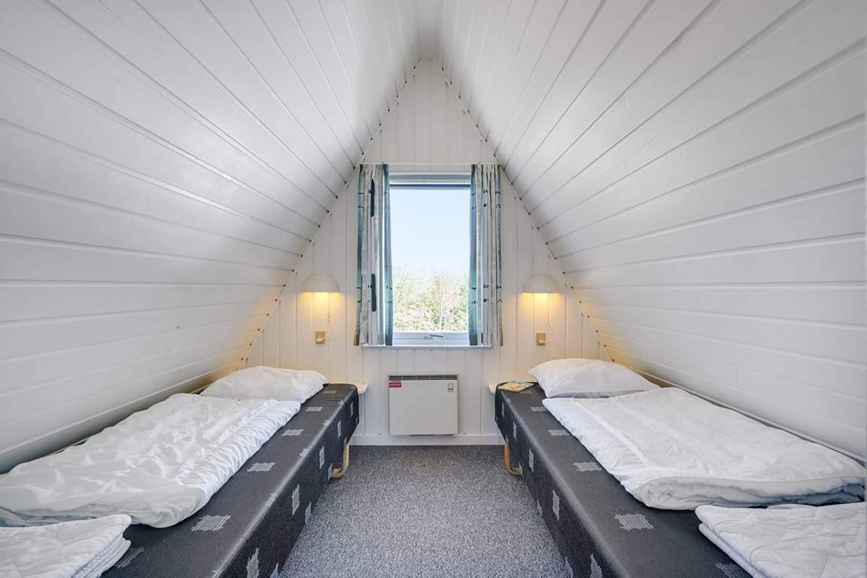 Una habitación pequeña y triangular con dos camas individuales, una ventana con cortinas y un radiador.