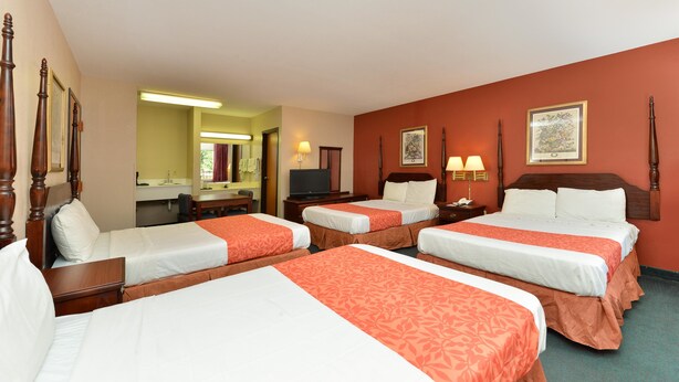 A hotel room with four beds, a desk, a television, and a bathroom. - Americas Best Value Inn & Suites Sheridan (Sheridan)