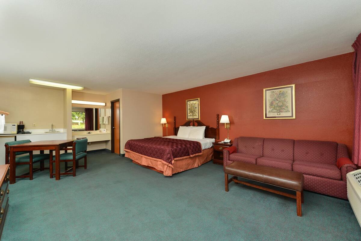Una habitación de hotel con cama, sofá, banco, escritorio con sillas y kitchenette.