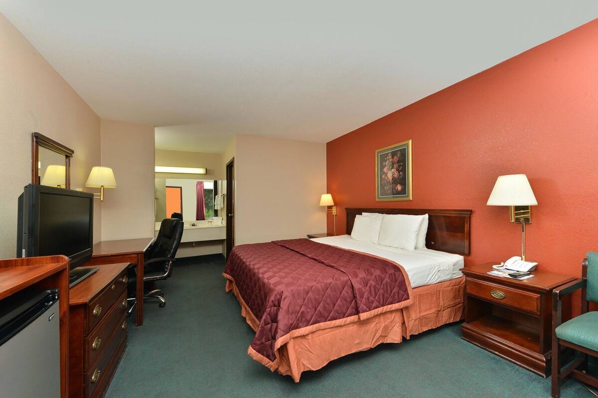 Habitación de hotel con cama, escritorio, silla, televisor y un cuadro en la pared.