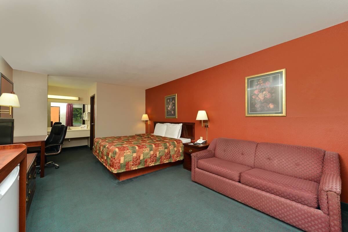Una habitación de hotel con cama, sofá, escritorio y silla, y dos lámparas de pared.