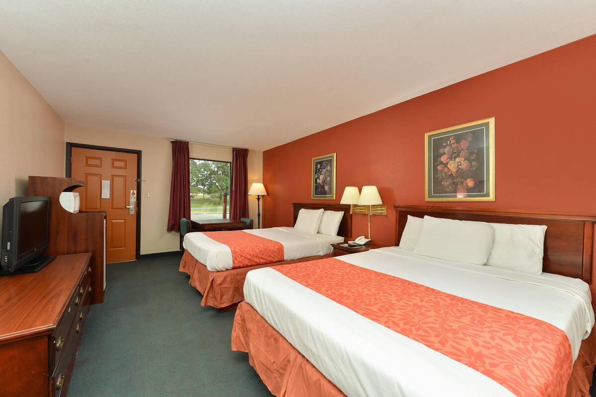 Habitación de hotel con dos camas, televisor, cómoda y ventana con cortinas.
