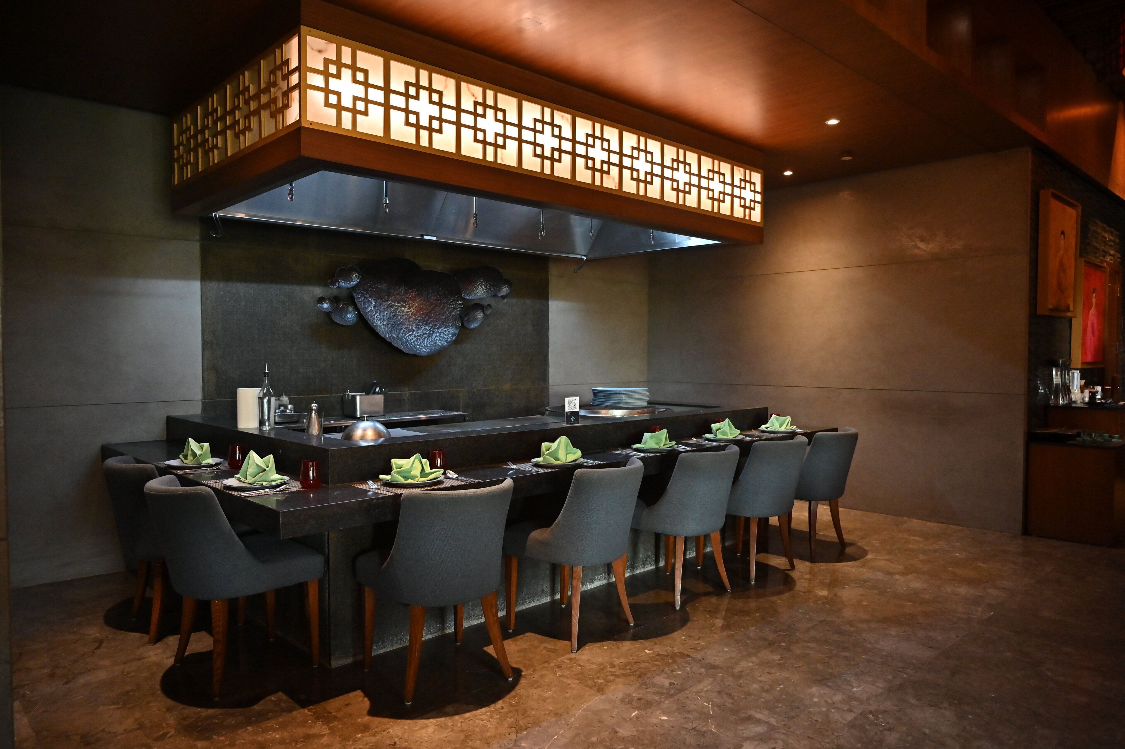 A modern restaurant with a long counter, multiple chairs, and a decorative ceiling.