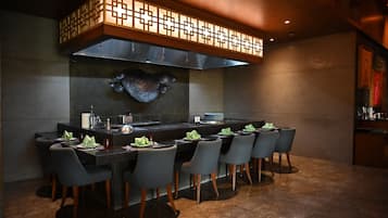 A modern restaurant with a long counter, multiple chairs, and a decorative ceiling.