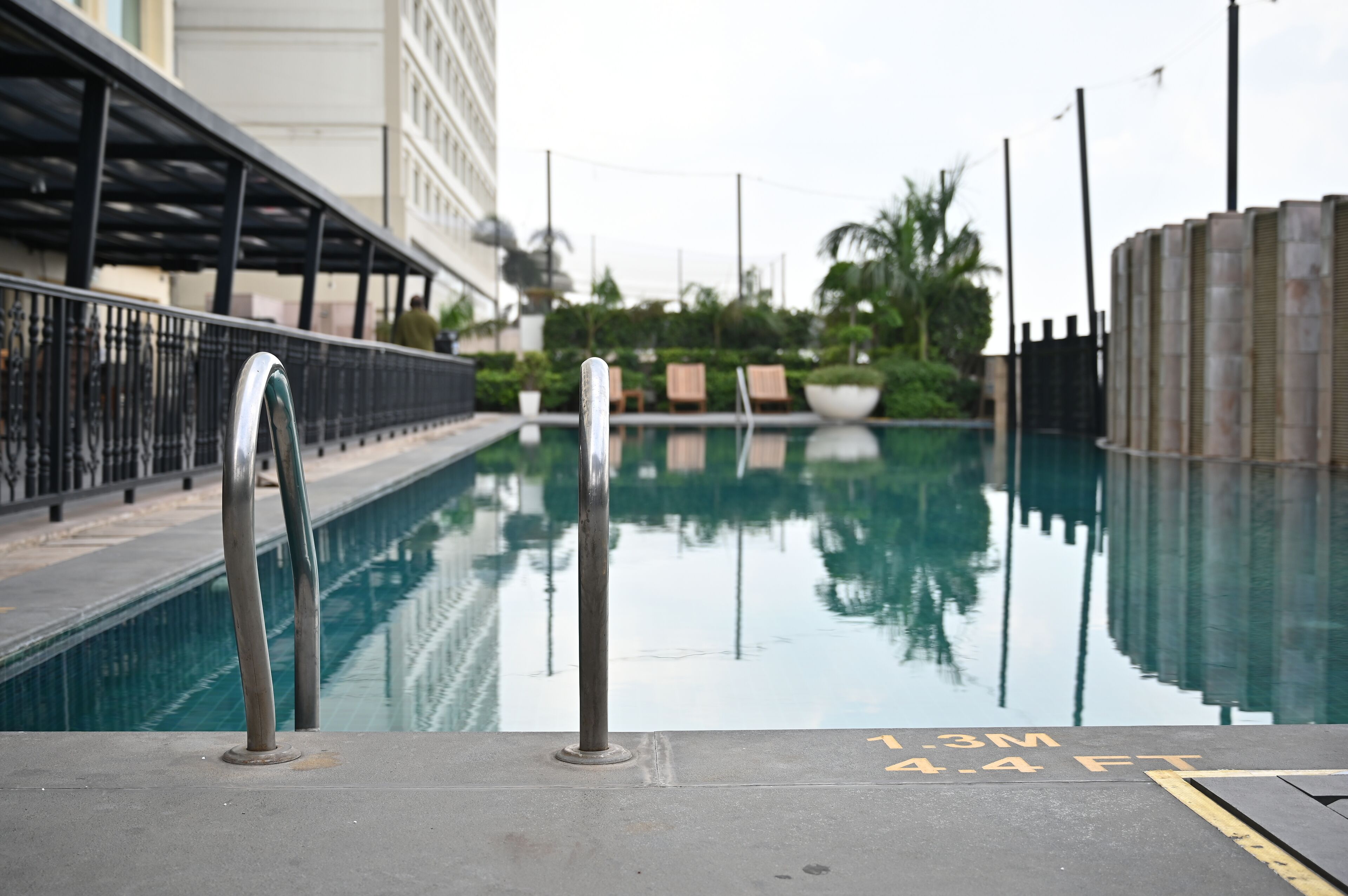 A swimming pool with a metal ladder, lounge chairs, and a palm tree in the background.
