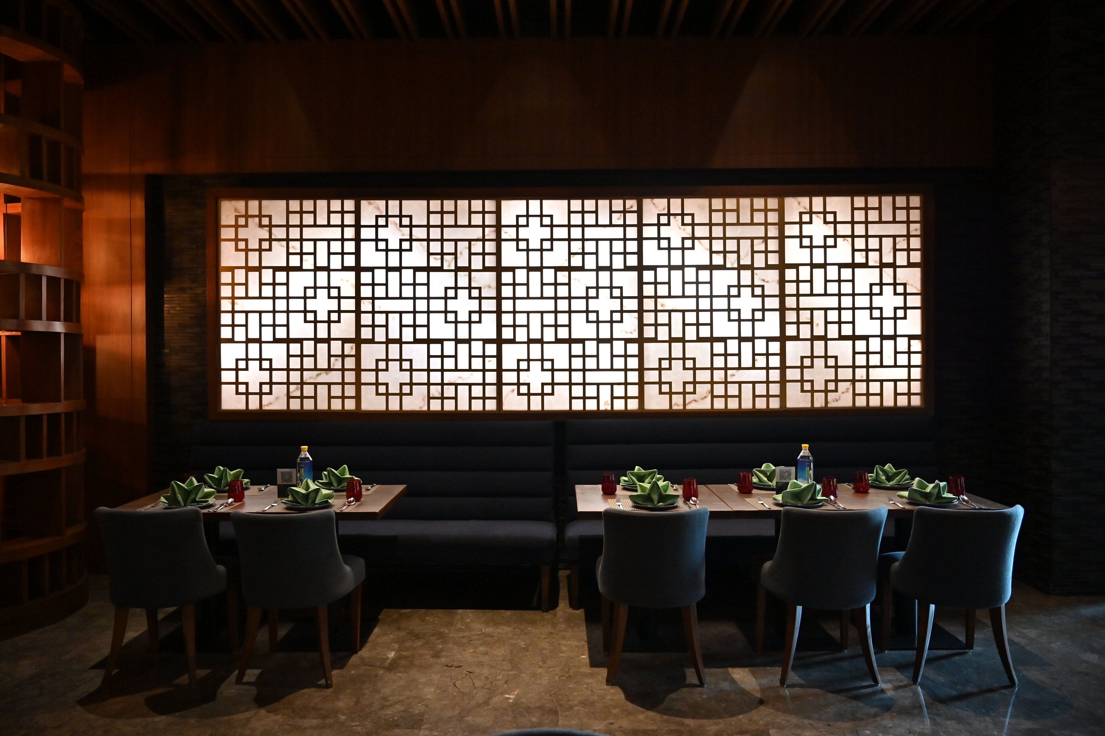 A restaurant with a dark interior, a large decorative screen, and a long table with chairs.