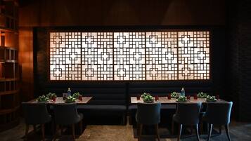 A restaurant with a dark interior, a large decorative screen, and a long table with chairs.