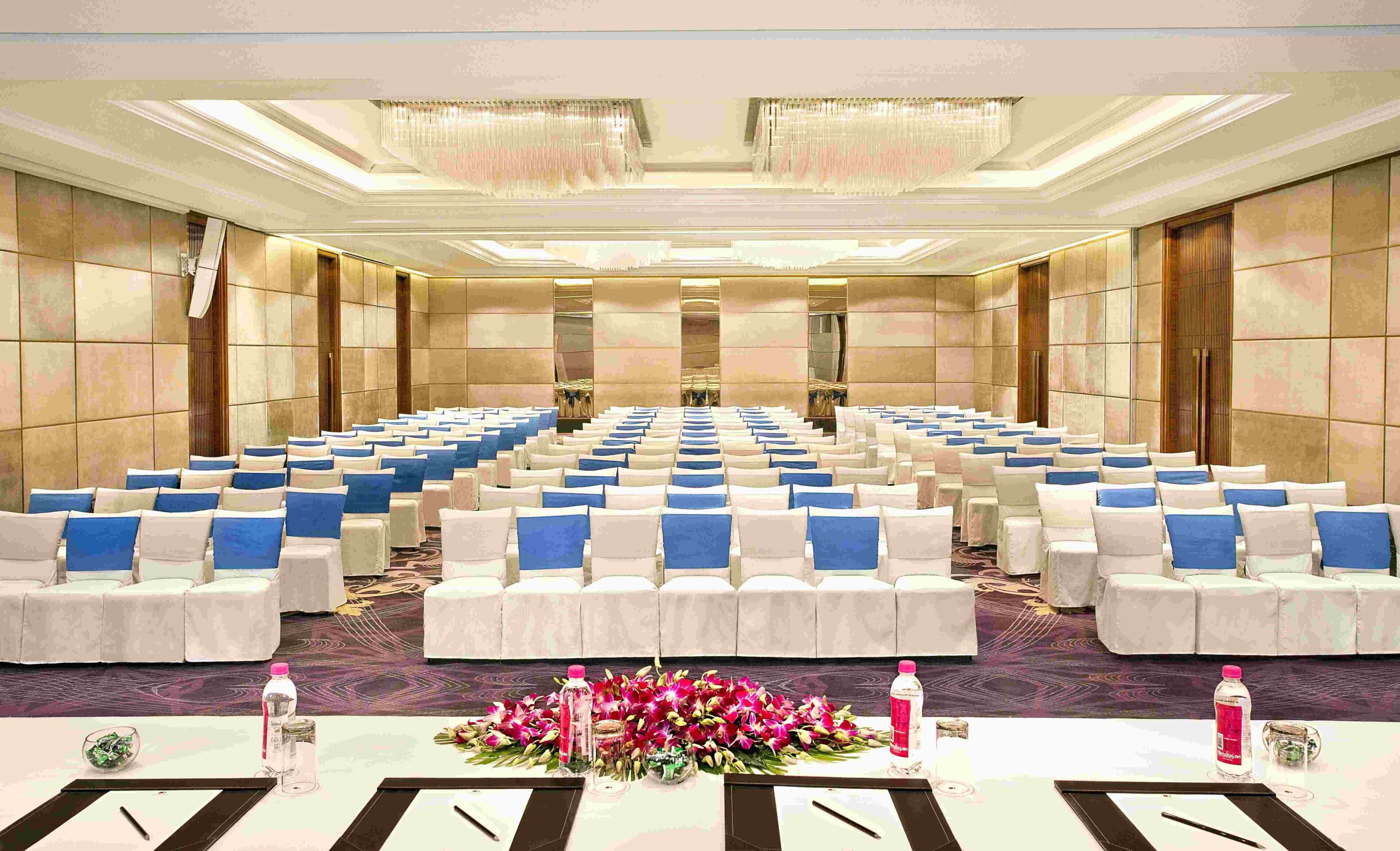 A conference room with rows of chairs, tables with water bottles and notepads, and a floral centerpiece.