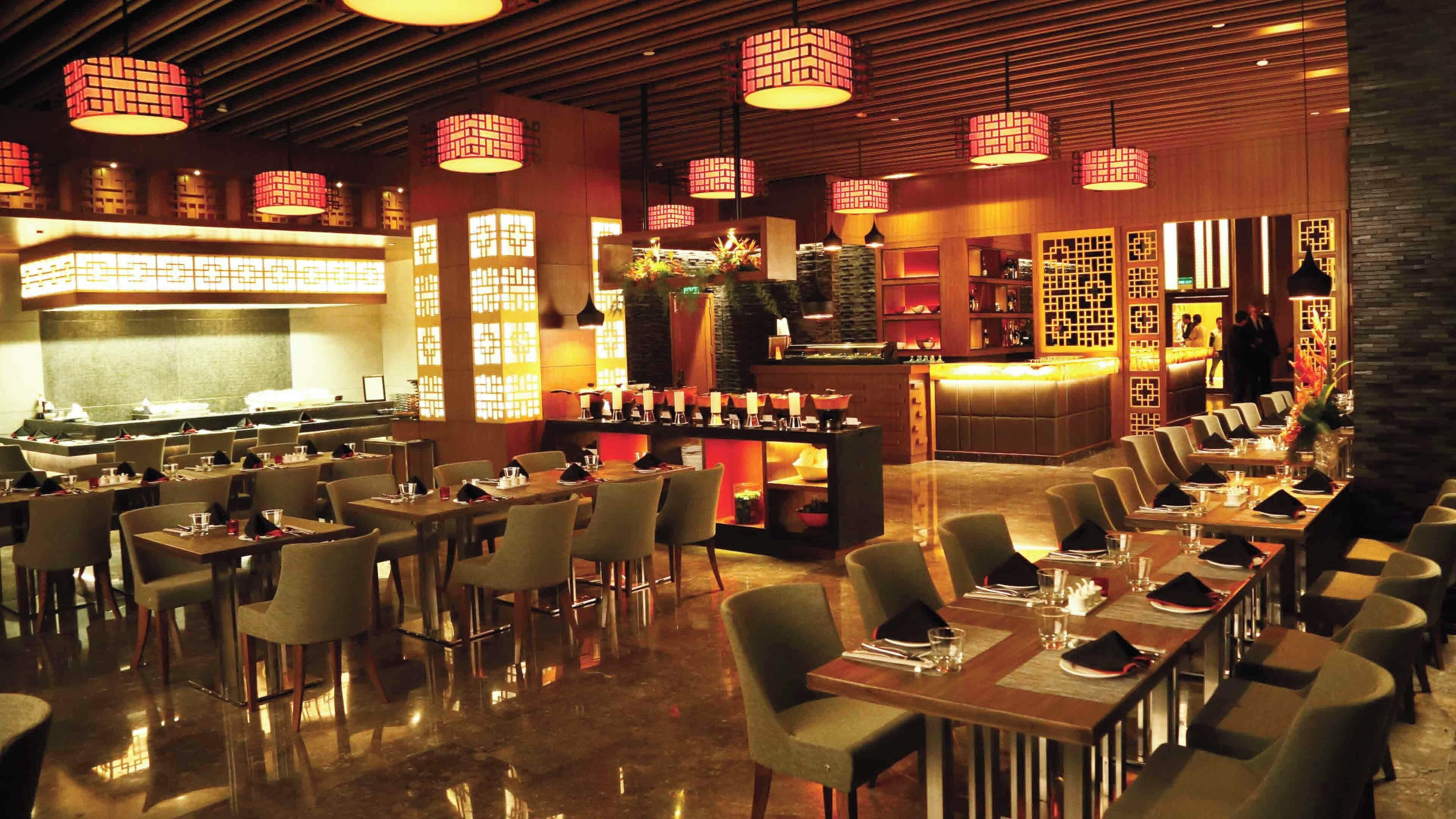 Un restaurante con varias mesas y sillas, una zona de bar e iluminación decorativa.