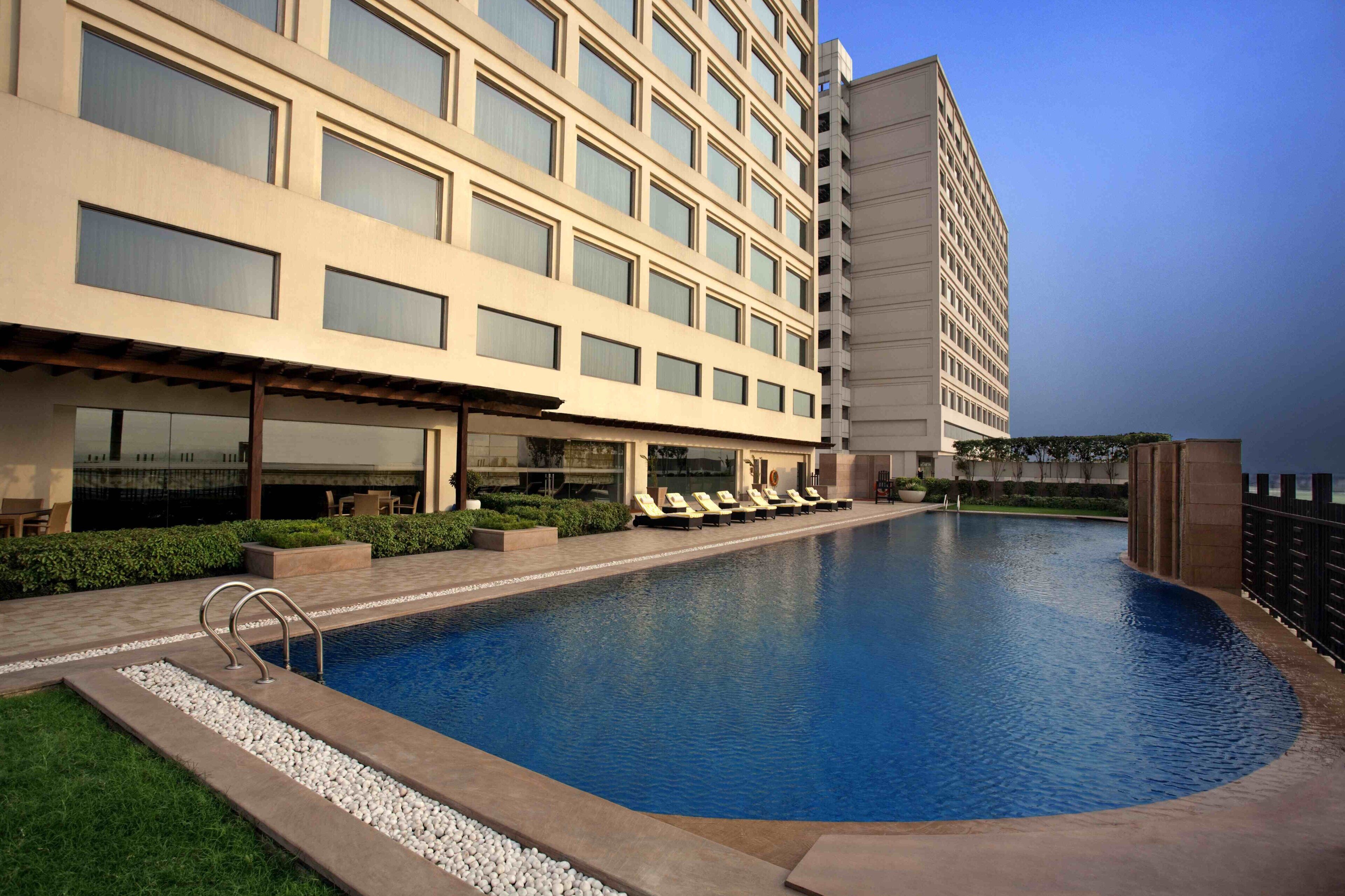 Un hotel con piscina, lettini e una zona salotto all'aperto coperta.