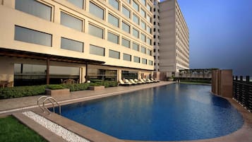 Un hotel con piscina, sillas de descanso y una zona de estar exterior cubierta.
