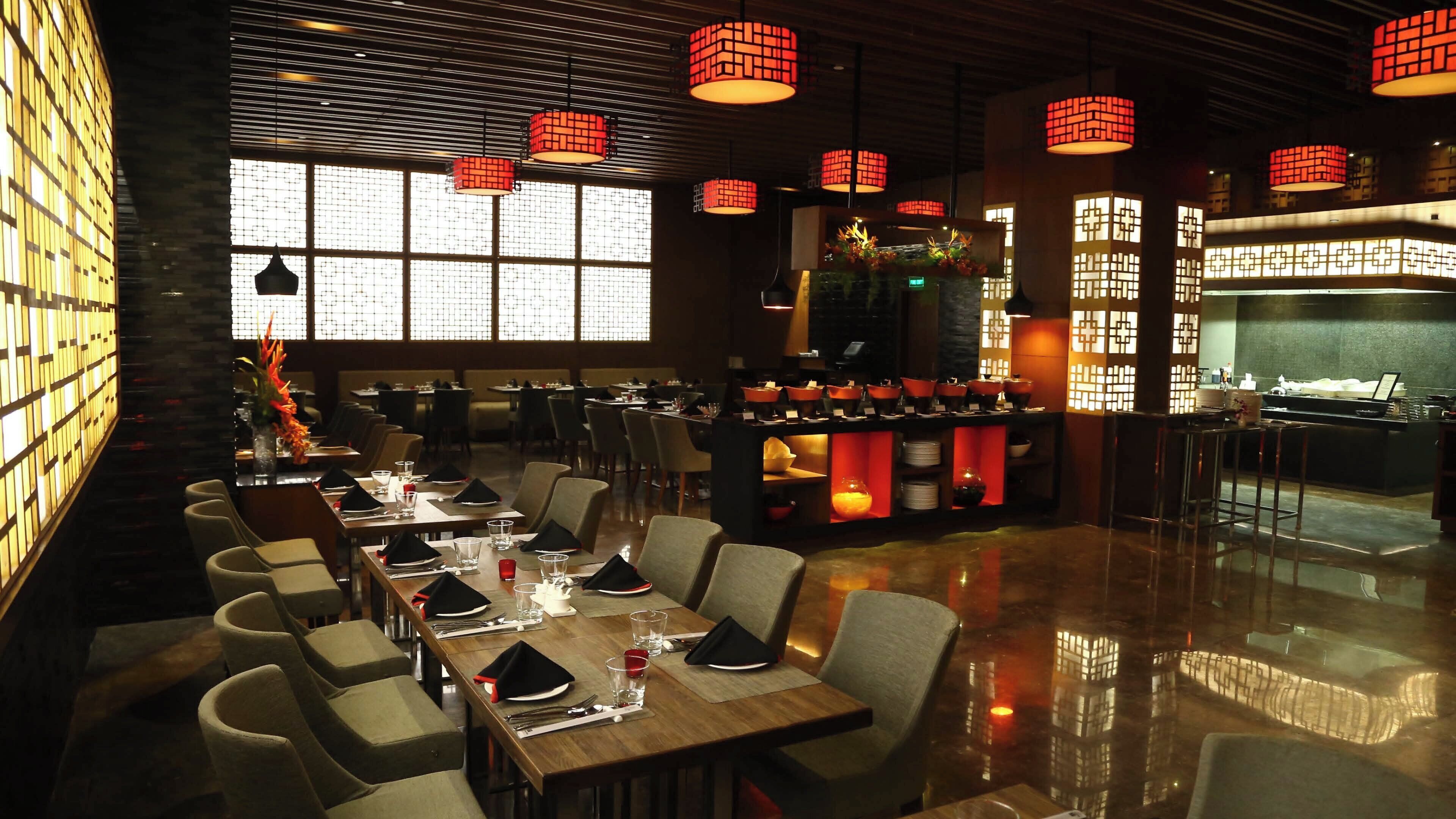 A restaurant with a long counter, multiple tables, and red hanging lamps.