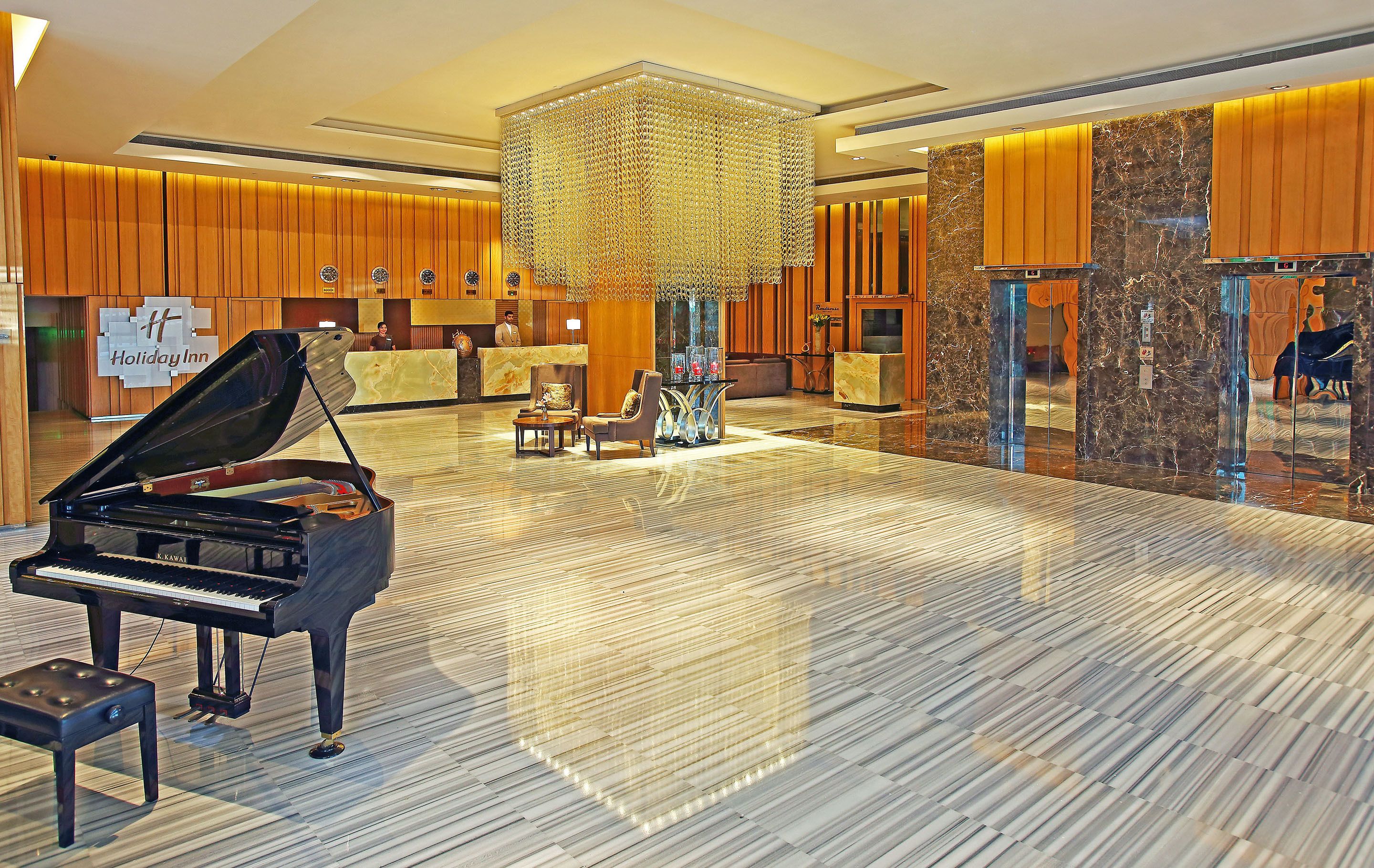 A grand piano in a spacious lobby with a reception desk, a large chandelier, and a marble floor.