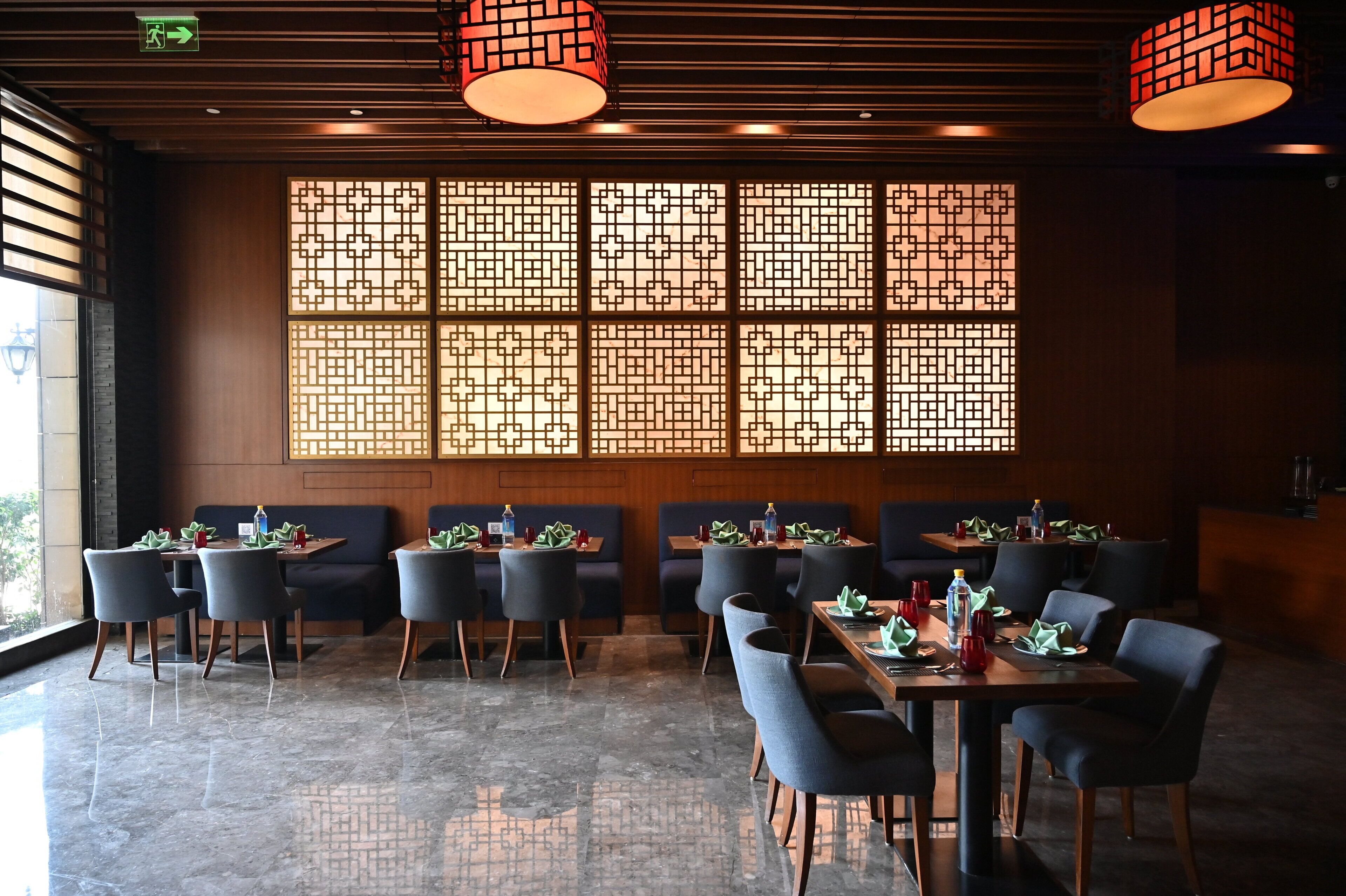 A restaurant with a traditional design, featuring wooden paneling, a large window with a geometric pattern, and a mix of seating options including tables and booths.