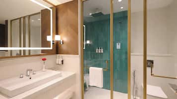 A modern bathroom with a large mirror, a white sink, a glass-enclosed shower, and a white toilet.
