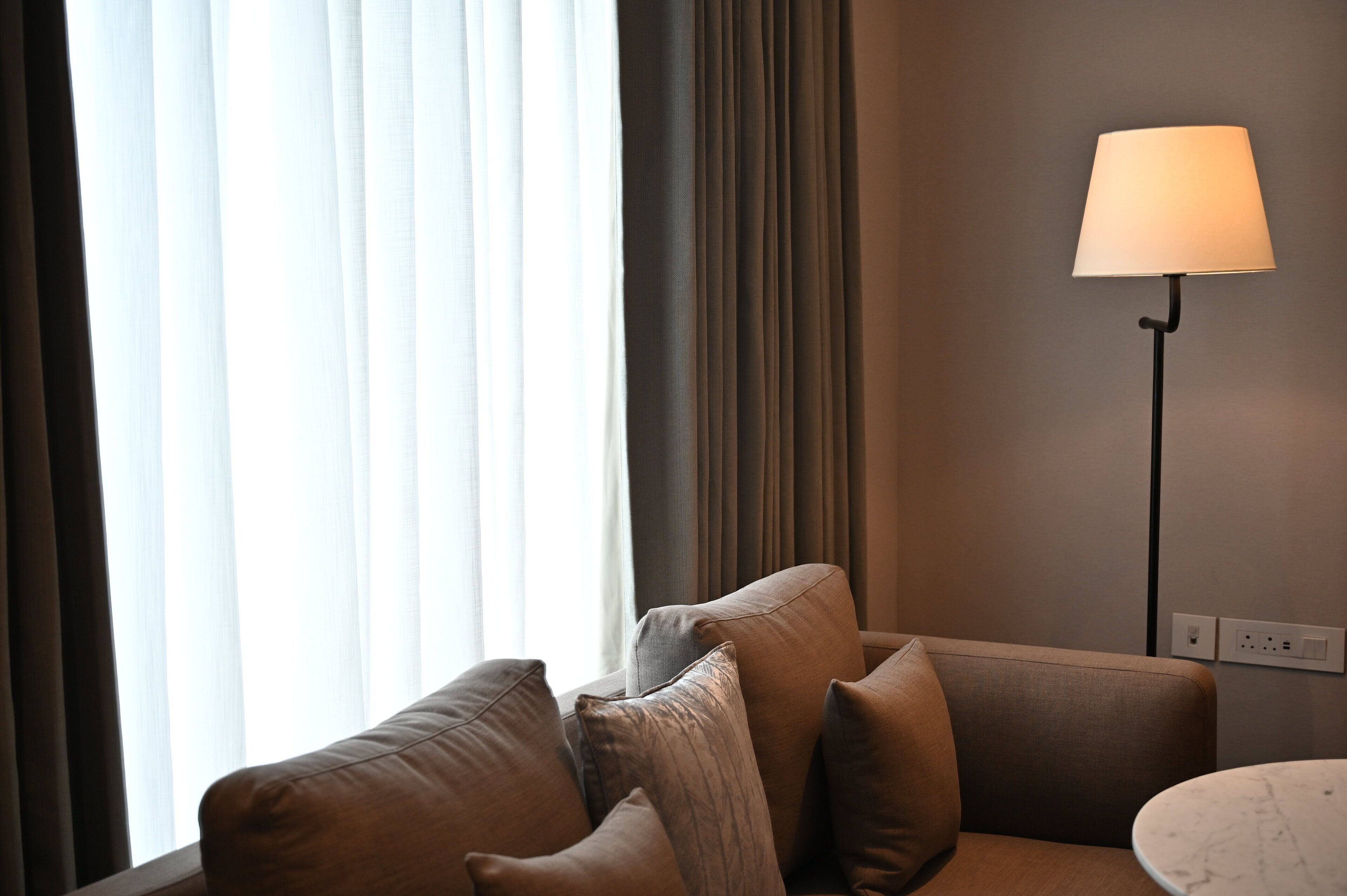 Una sala de estar moderna con un sofá, una lámpara y vistas a una ventana con cortinas.