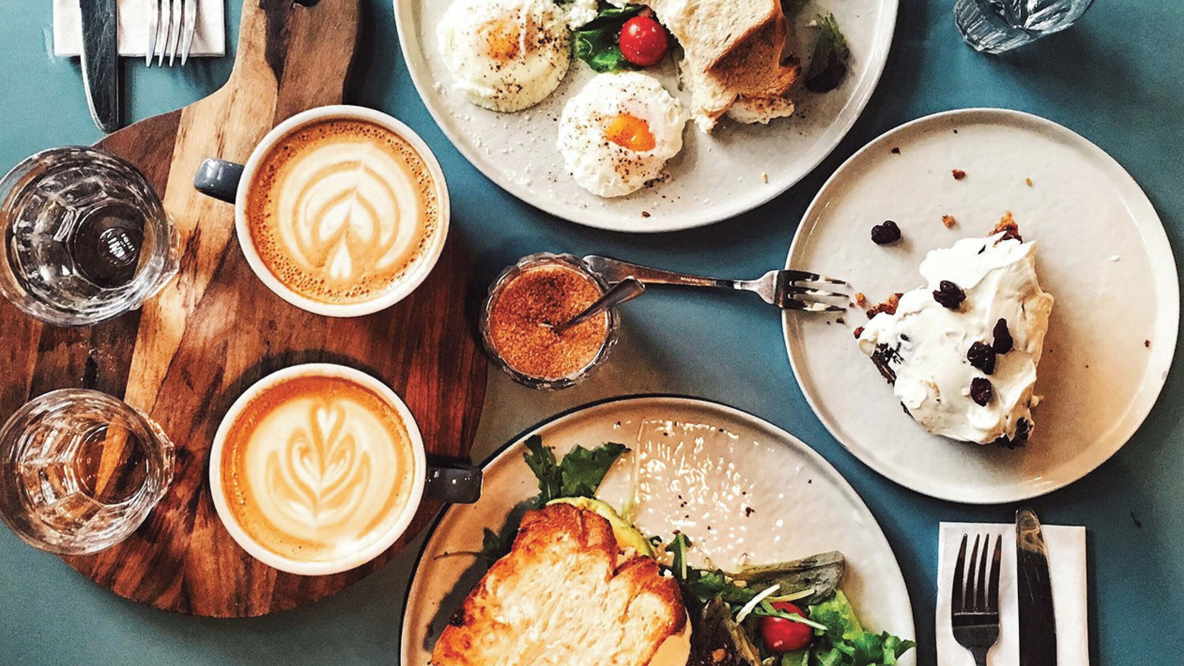 A table with various dishes, including eggs, a salad, and a dessert, along with cups of coffee.
