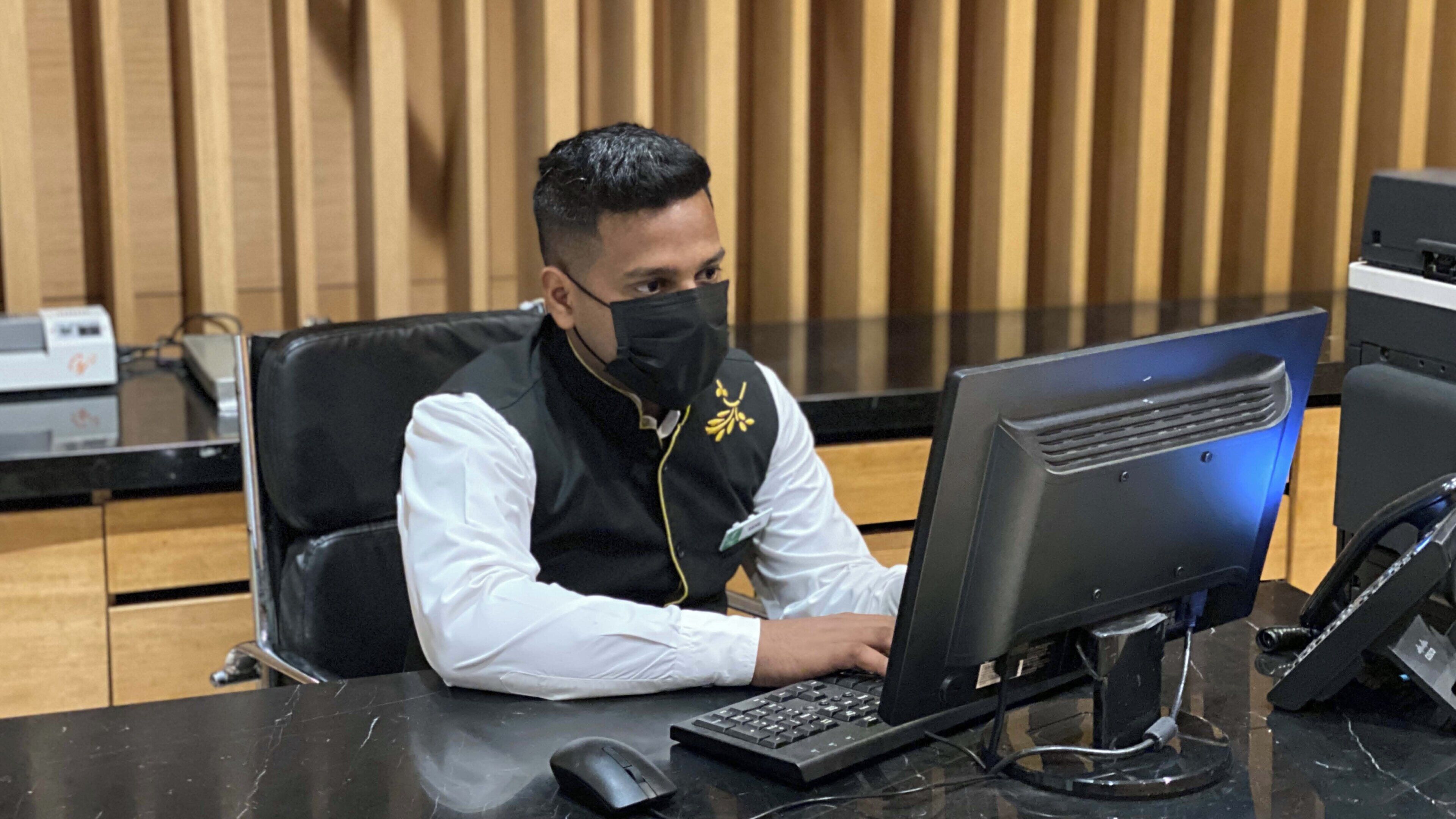 A person seated at a desk with a computer, a telephone, and a keyboard.