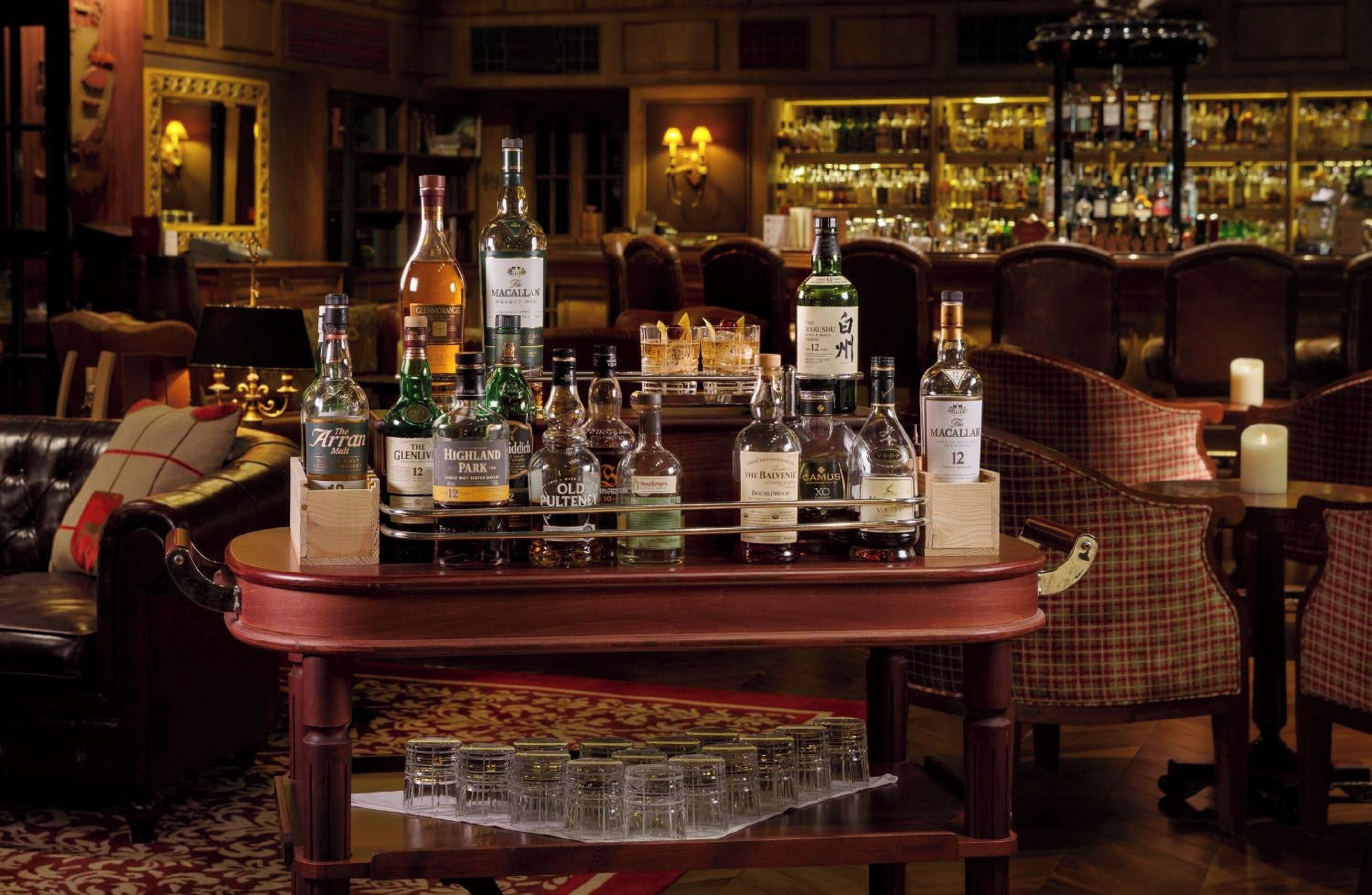 Una zona de bar con una variedad de botellas de licores y vasos sobre una barra de madera.