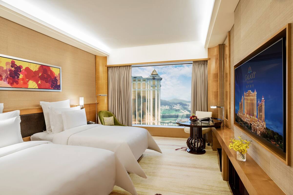 Une chambre d’hôtel avec deux lits, une grande fenêtre donnant sur un beau paysage, un bureau avec une chaise et un téléviseur fixé au mur.