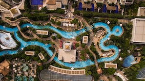 An aerial view of a resort with multiple interconnected swimming pools, lush landscaping, and a variety of amenities including sun loungers and umbrellas. - Galaxy Hotel (Cotai)