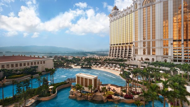 A resort with multiple swimming pools, a large building with arched windows, and a view of distant mountains. - Galaxy Hotel (Cotai)