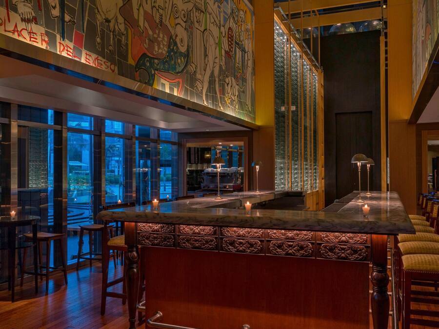 A bar area with a high ceiling, large windows, and a mural on the wall.