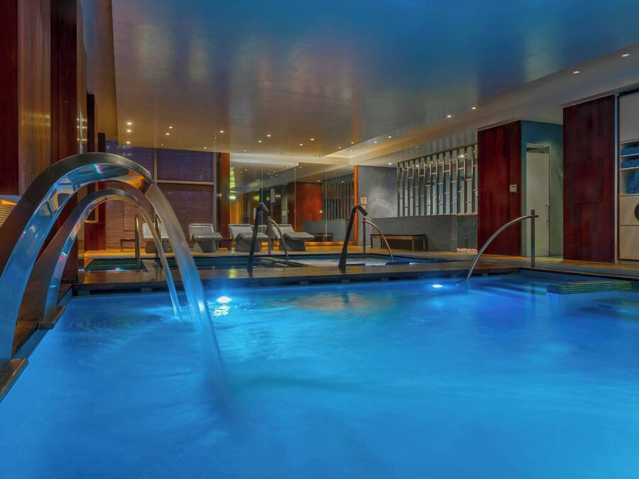 An indoor swimming pool with clear water, surrounded by wooden paneling and modern lighting fixtures.
