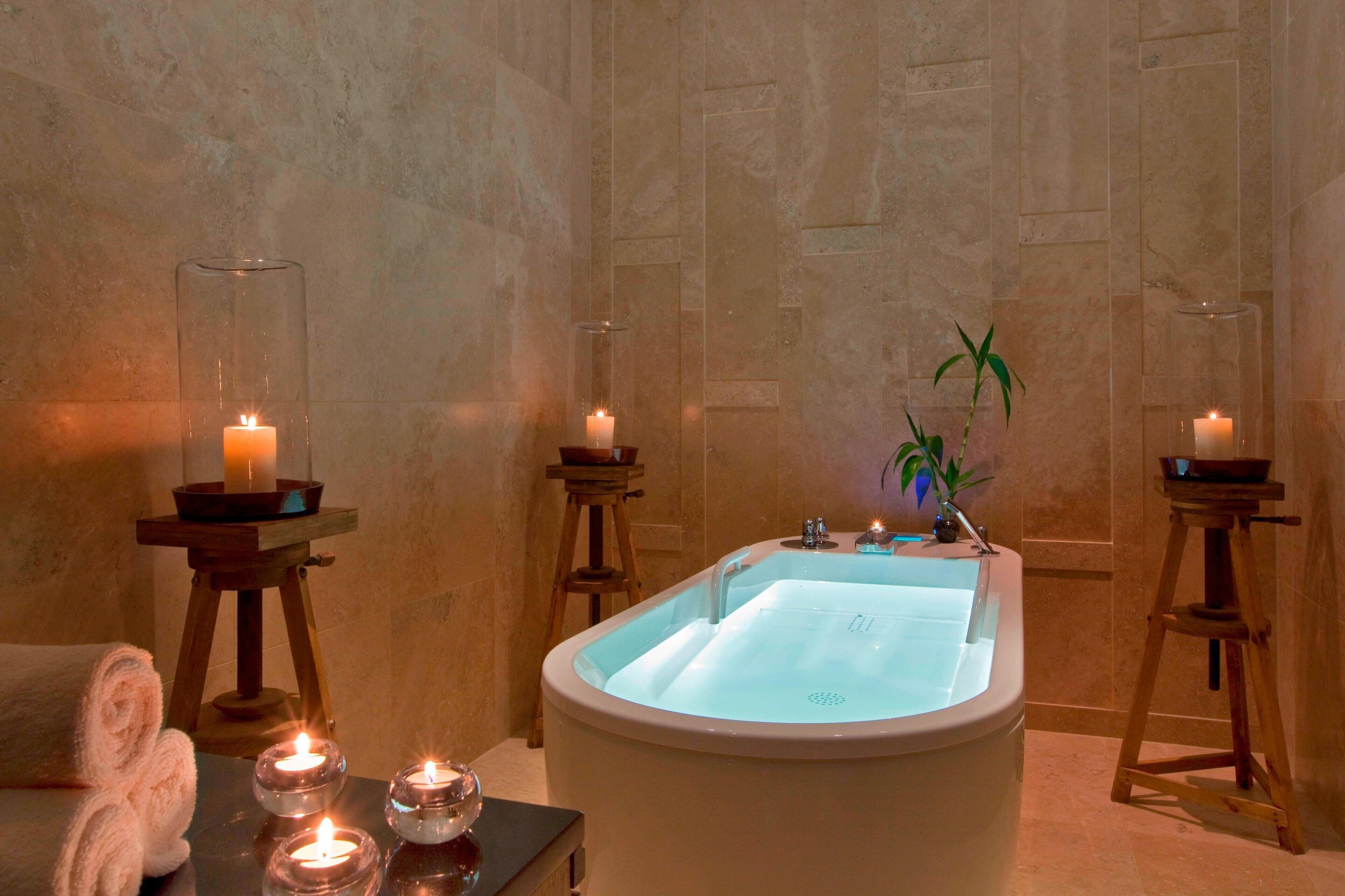 Une salle de spa avec une grande baignoire, des bougies et une petite plante.