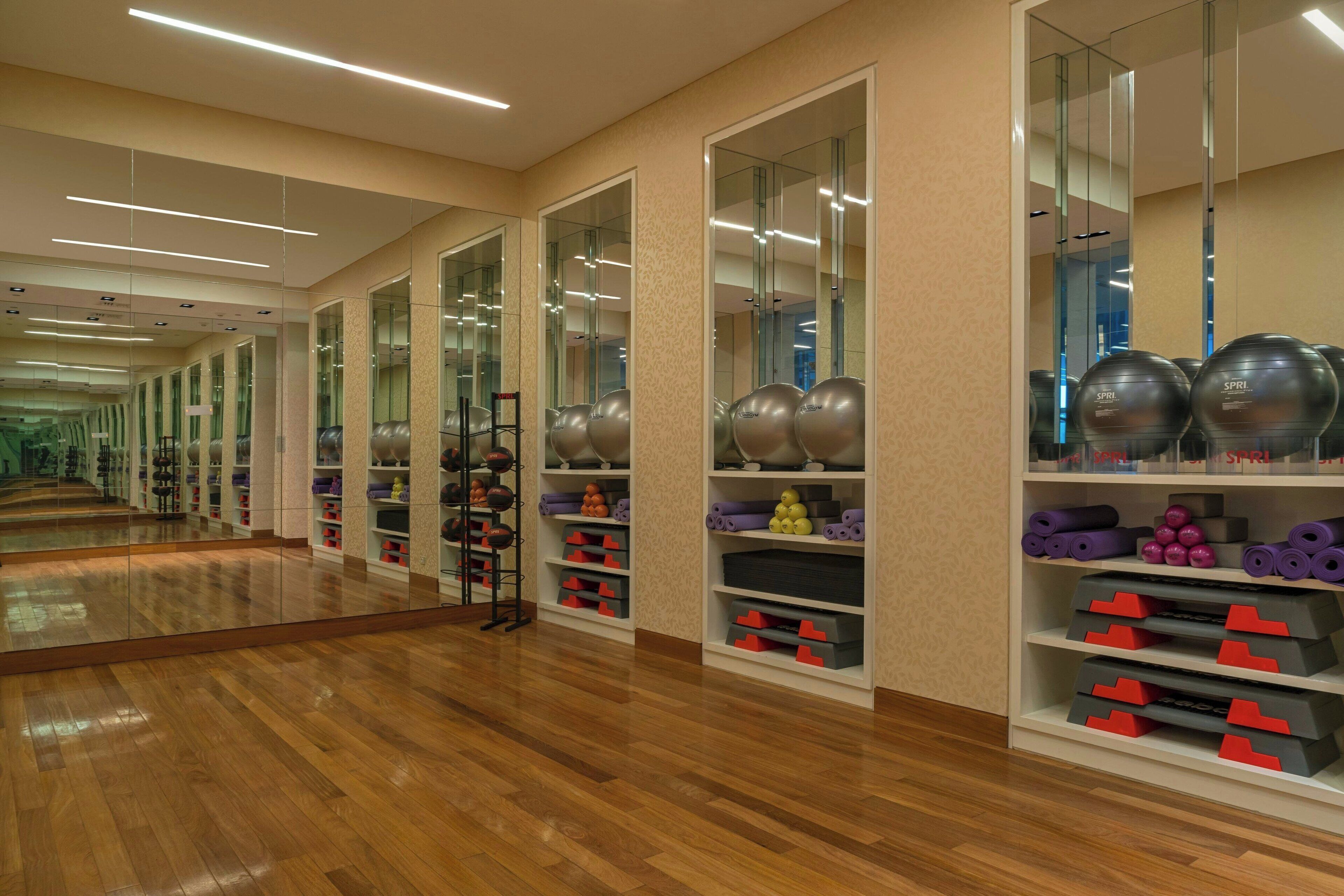 Een sportschool met spiegelwanden, houten vloeren en diverse fitnessapparaten.