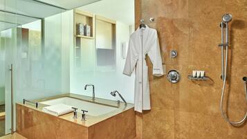 A modern bathroom with a large mirror, a glass-enclosed shower, a white robe hanging on the wall, and a marble-tiled floor.