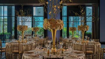 A banquet hall with round tables set for a formal event, featuring gold accents and floral centerpieces.