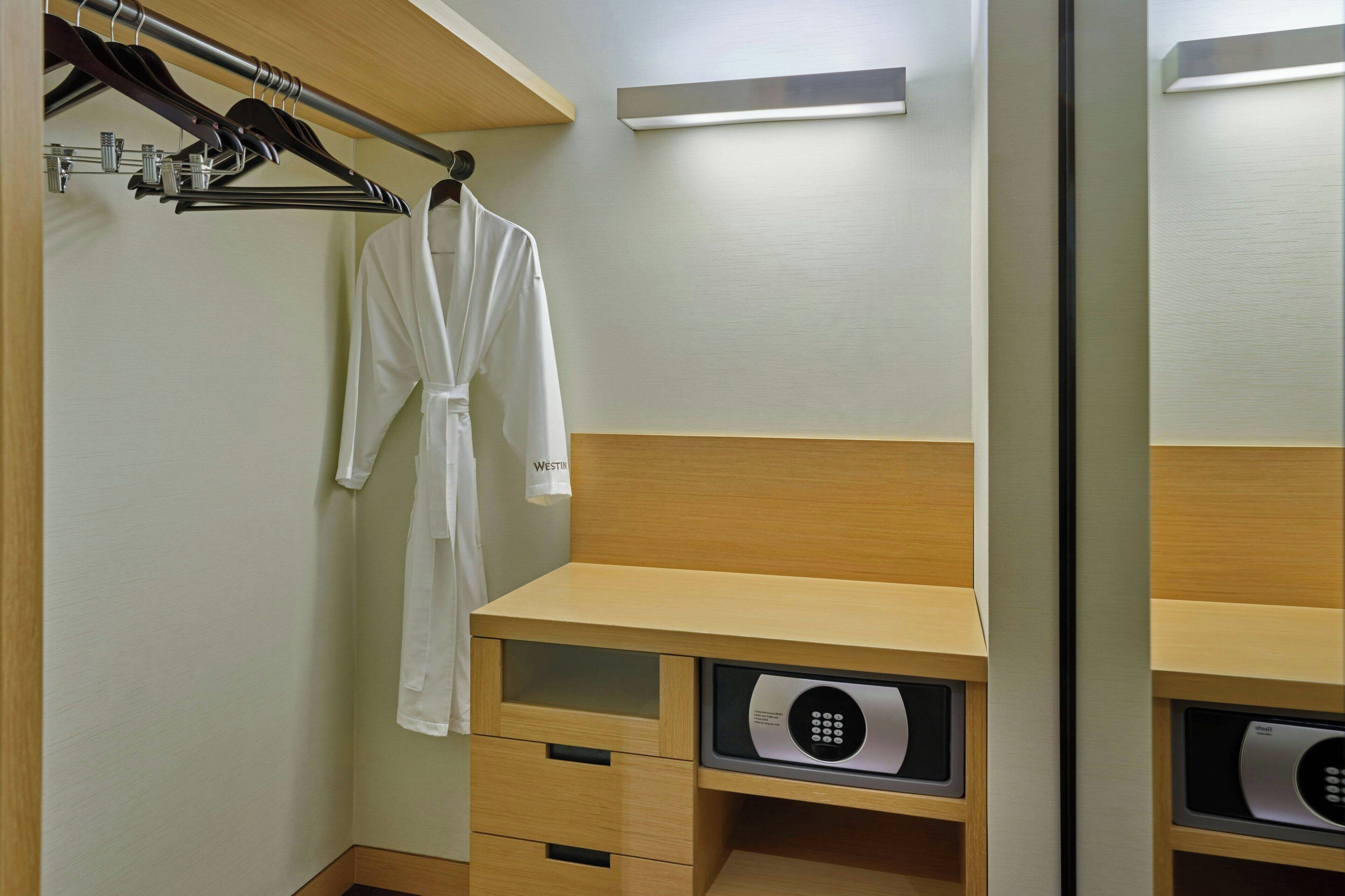 A hotel room with a wooden vanity, a robe hanging on a rack, and a minibar with a digital lock.