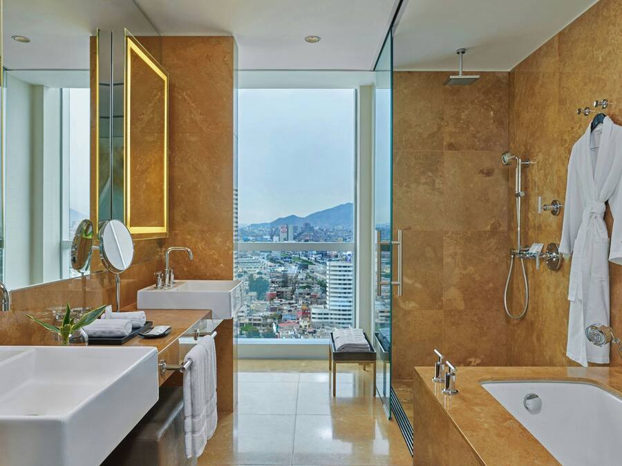 Een moderne badkamer met dubbele wastafels, een grote spiegel, een douche en uitzicht op een stadsgezicht.