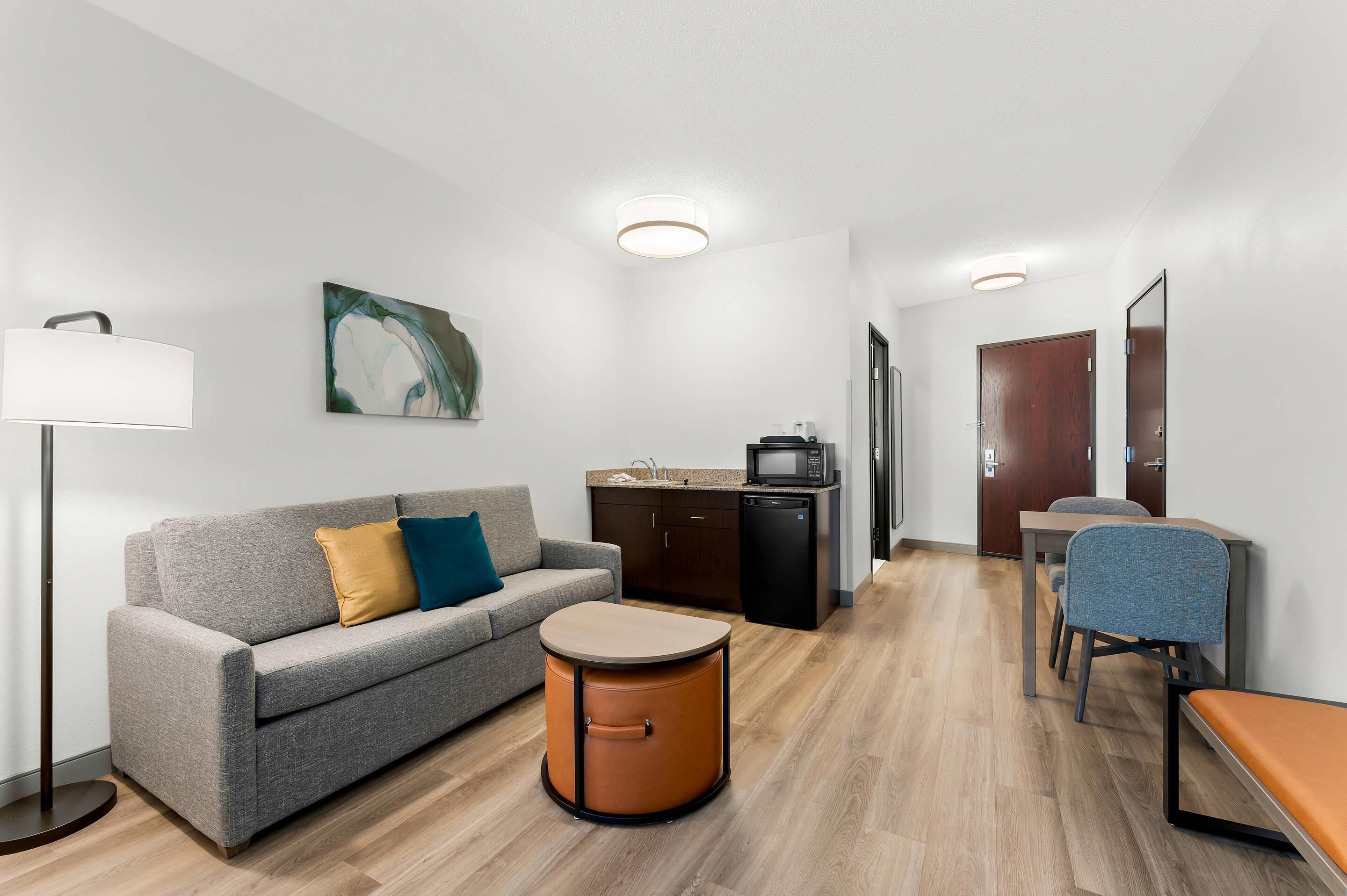 Una habitación de hotel moderna con sofá, una mesita redonda, un escritorio con silla, microondas y armario.