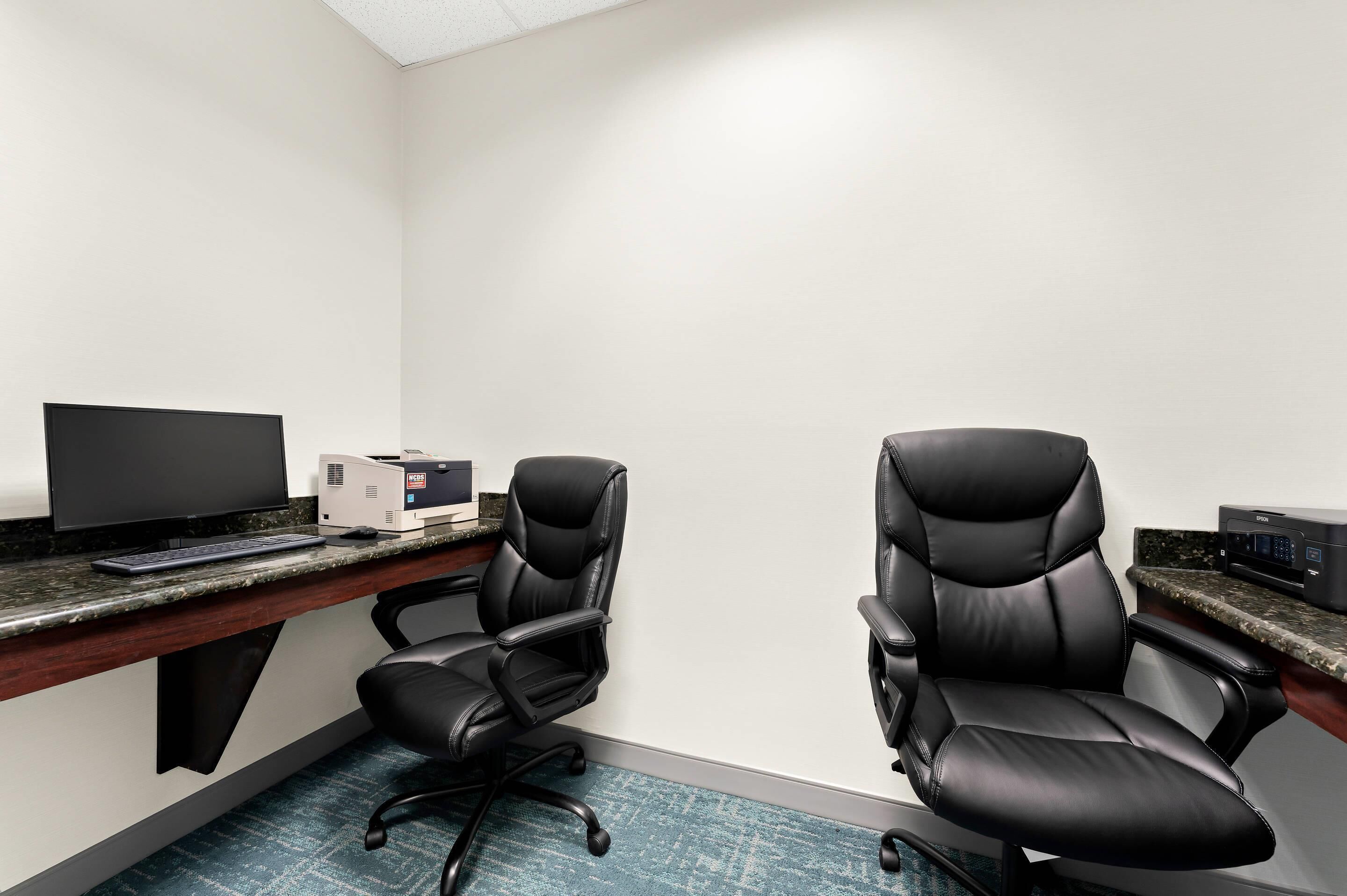 A room with a desk, two black office chairs, a computer monitor, and a printer.