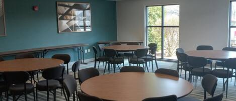 Un salón de conferencias con mesas y sillas redondas, un ventanal grande y una pared de acento color verde azulado.
