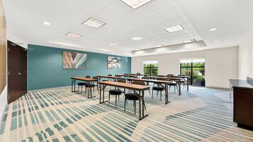 A conference room with multiple tables and chairs, a large window, and a carpeted floor.