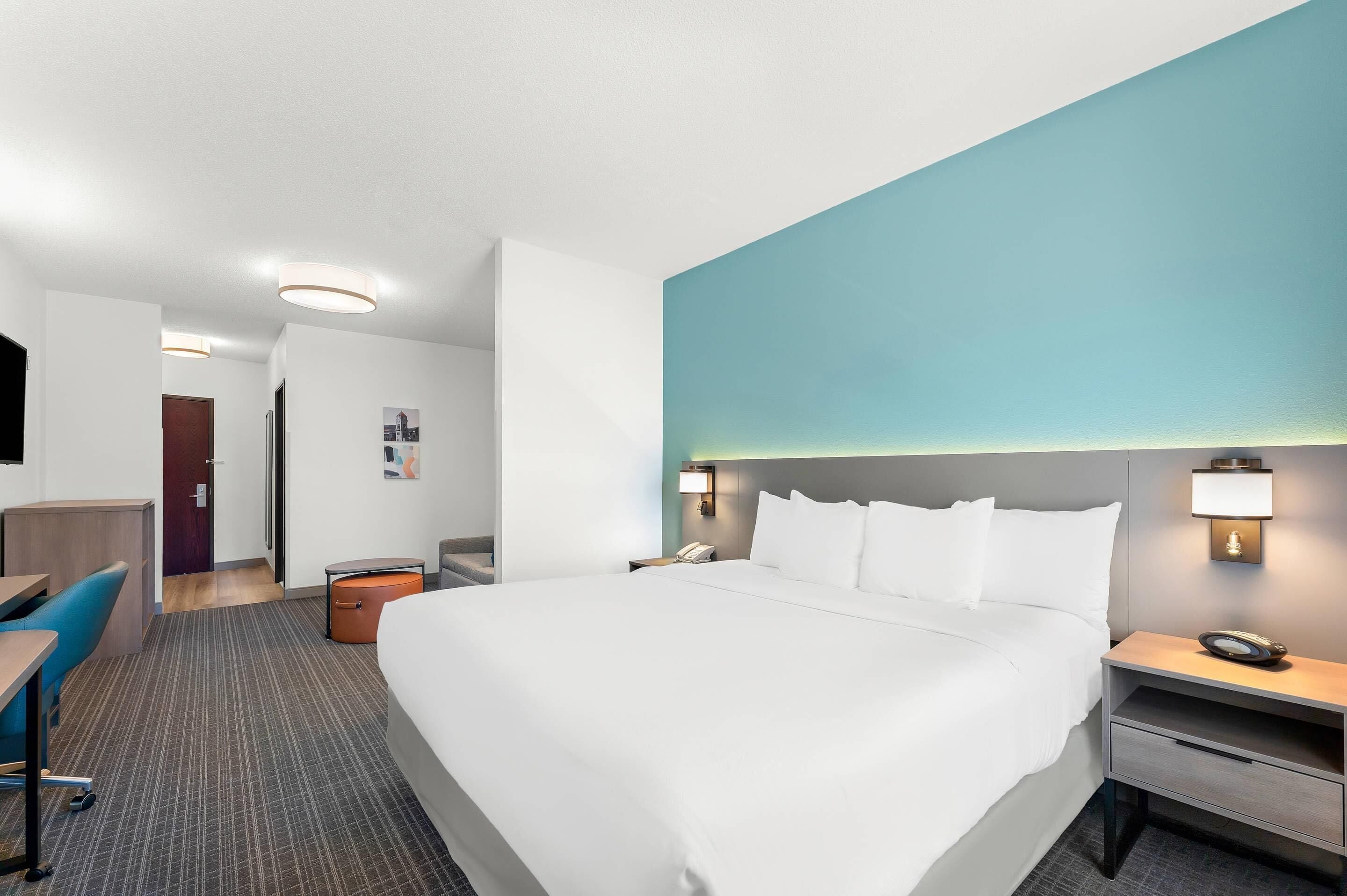 Une chambre d’hôtel avec un grand lit, un bureau, une chaise, une table de chevet et une lampe fixée au mur.