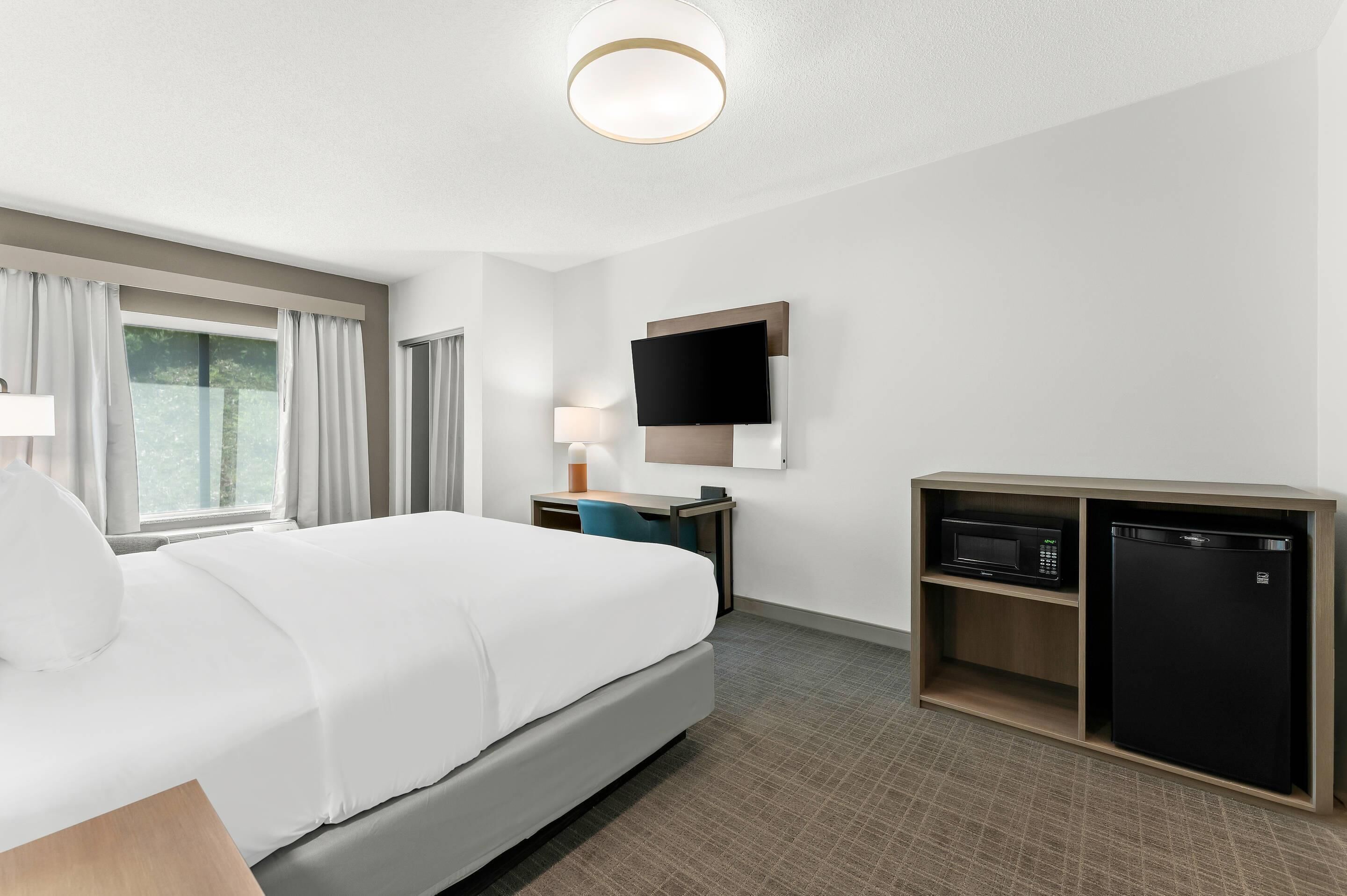 Habitación de hotel con cama, escritorio, computadora, televisor y minibar.