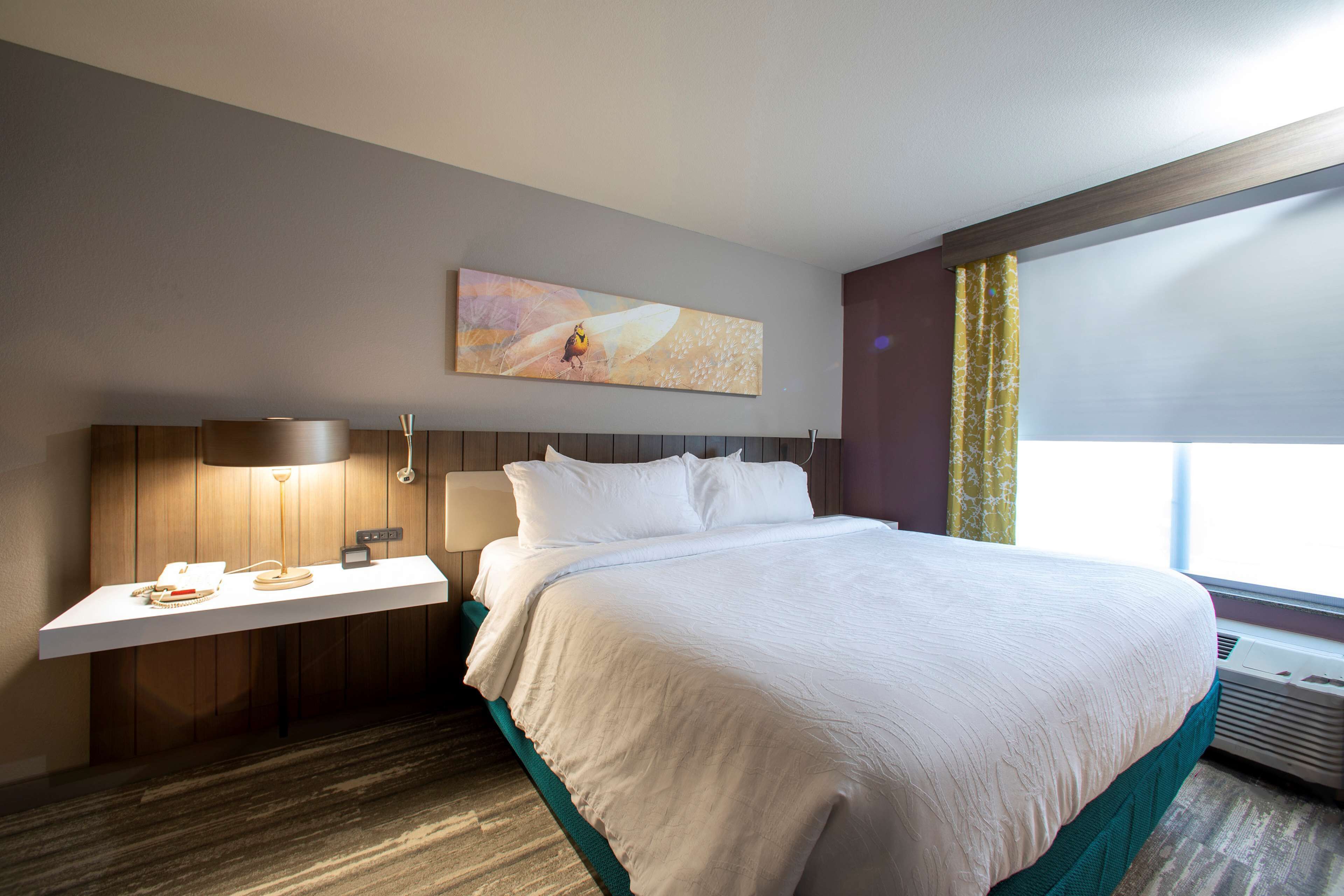 A hotel room with a bed, bedside table, lamp, and a painting on the wall.